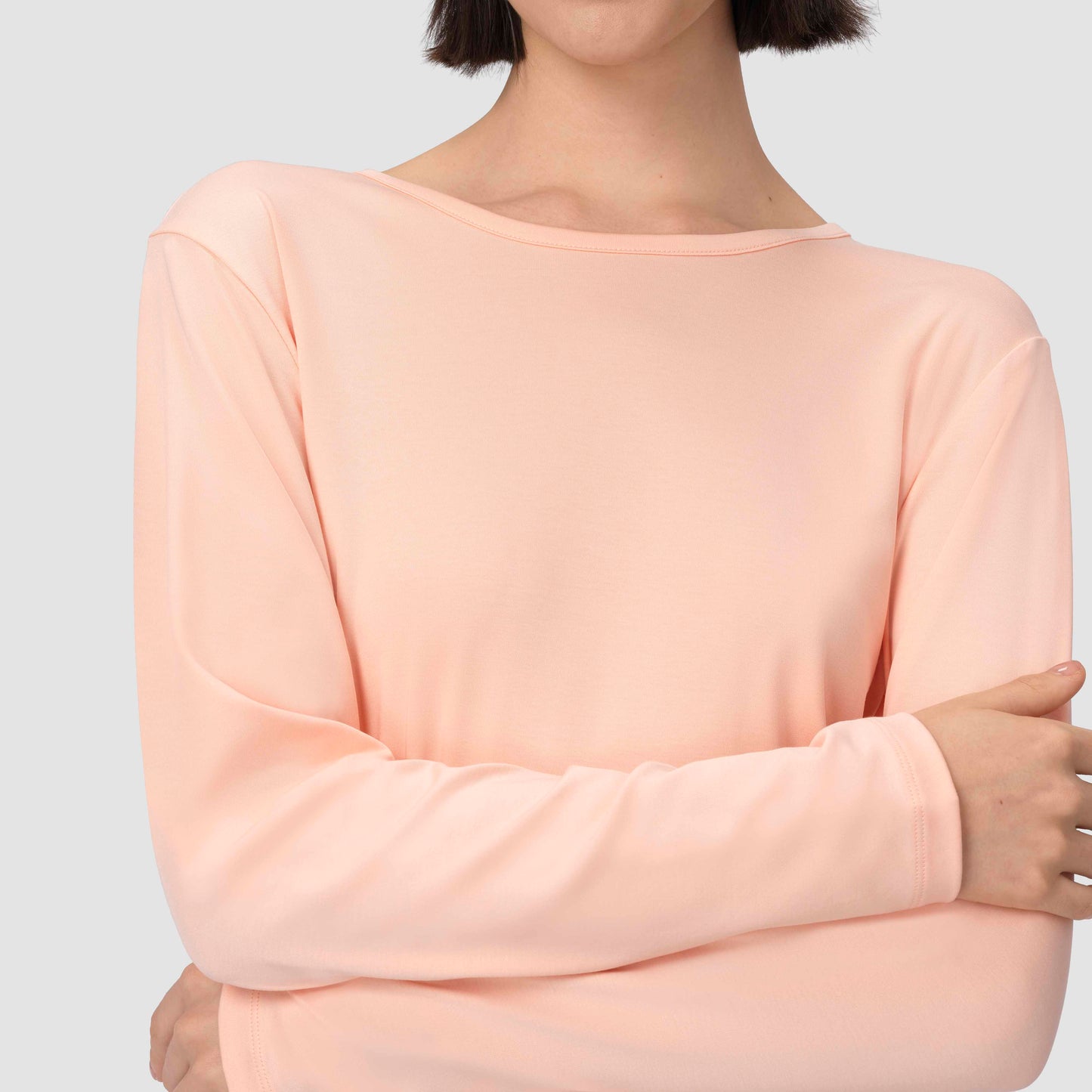 Person wearing a salmon light pink long-sleeve top against a plain background