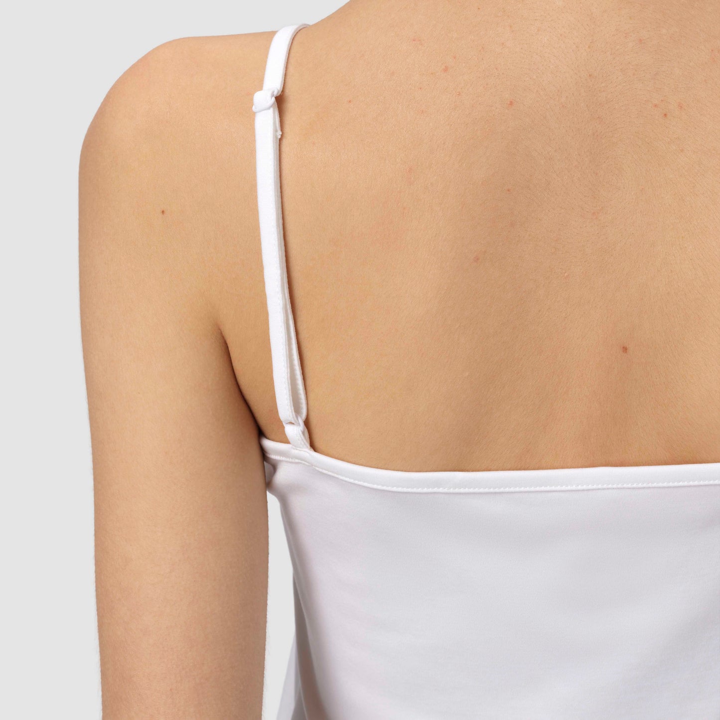 White spaghetti strap top worn by a person on a light gray background