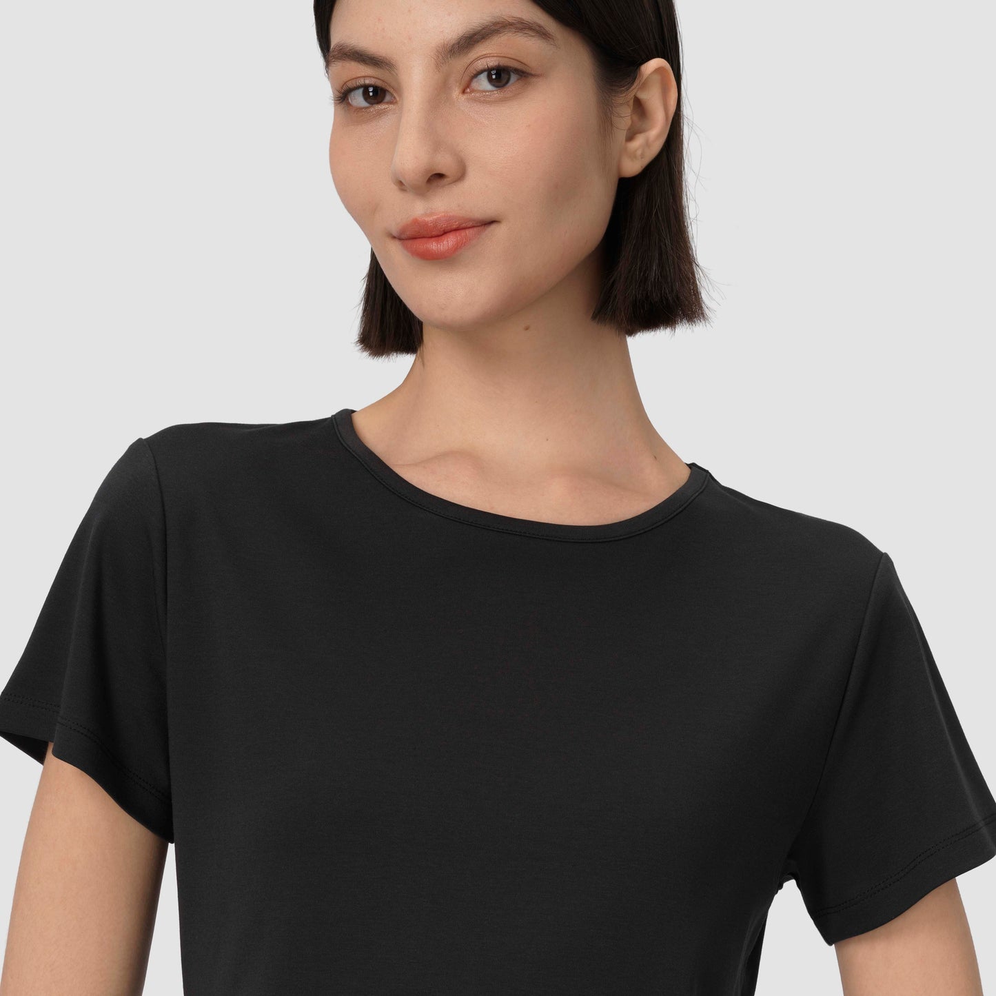 Une femme vêtue d'un t-shirt noir sur un fond uni