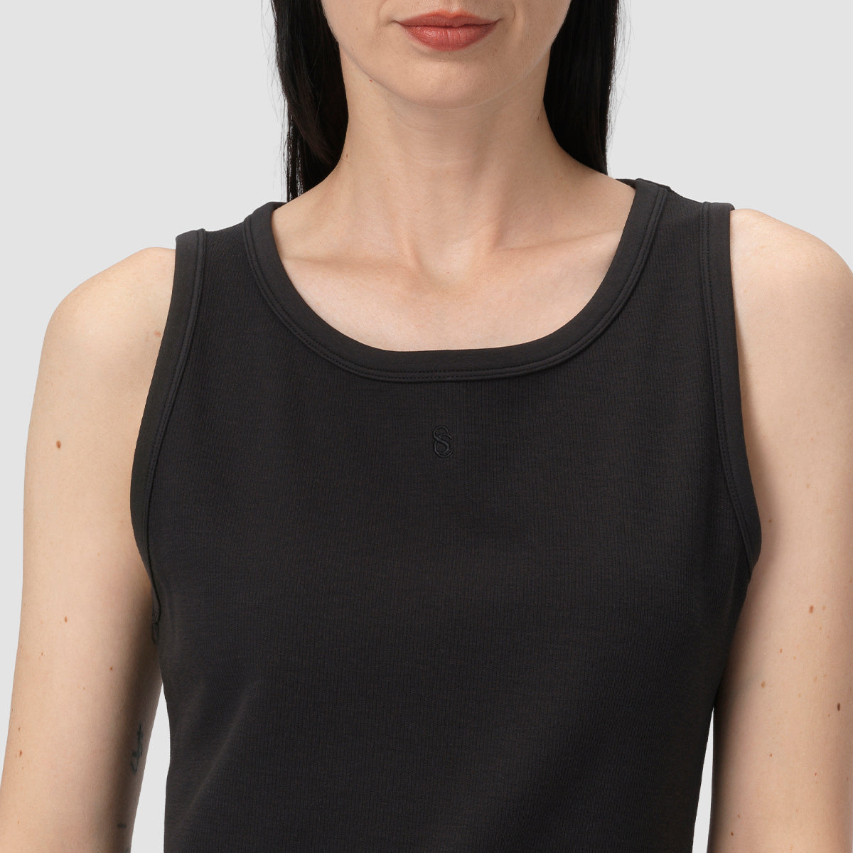 Woman wearing a black tank top against a plain background