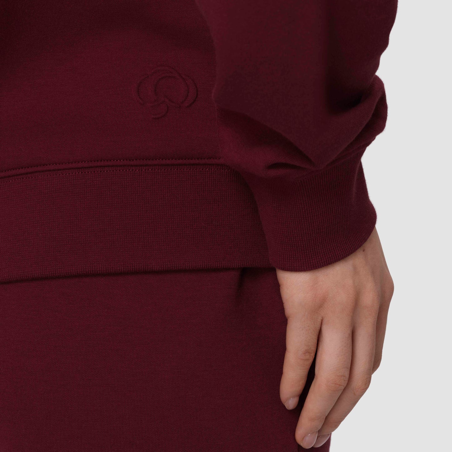 Gros plan sur un sweat-shirt bordeaux arborant le logo de la marque sur un fond gris clair