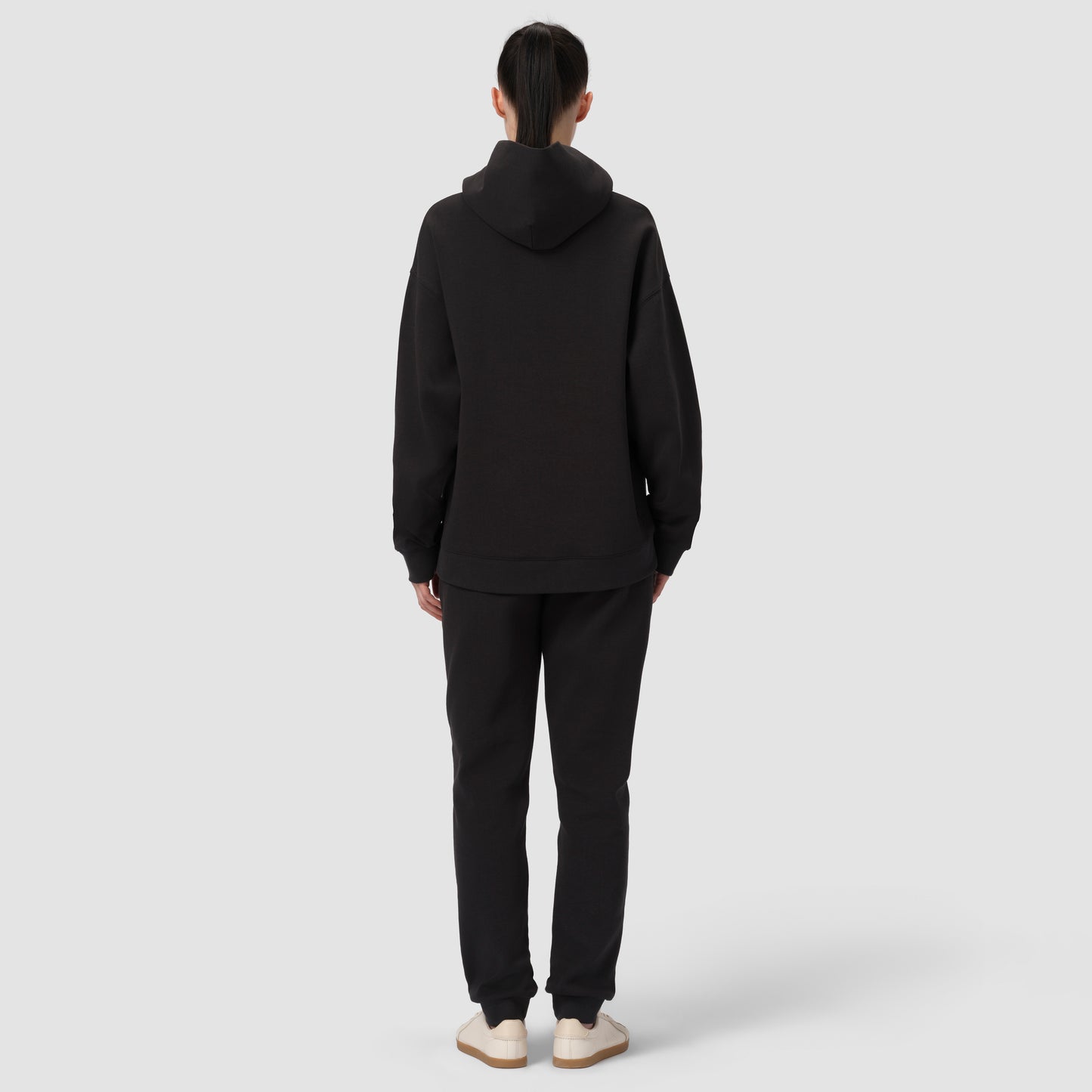 Une personne vêtue d'un sweat à capuche et d'un pantalon noirs sur fond blanc