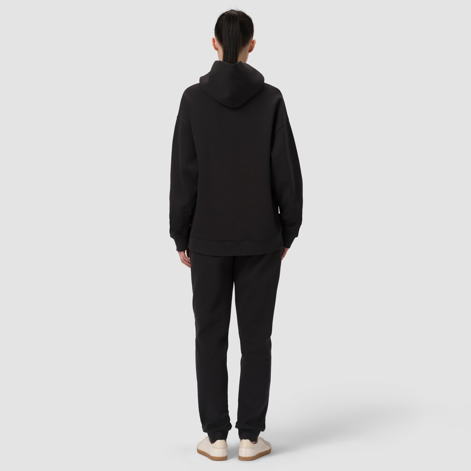 Une personne vêtue d'un sweat à capuche et d'un pantalon noirs sur fond blanc