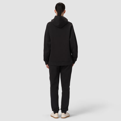 Une personne vêtue d'un sweat à capuche et d'un pantalon noirs sur fond blanc