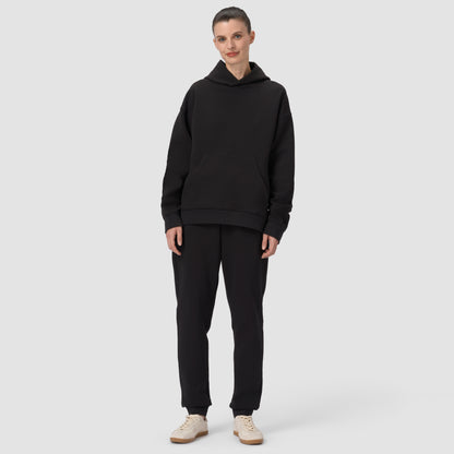 Une personne vêtue d'un ensemble sweat à capuche et pantalon noir sur fond gris clair