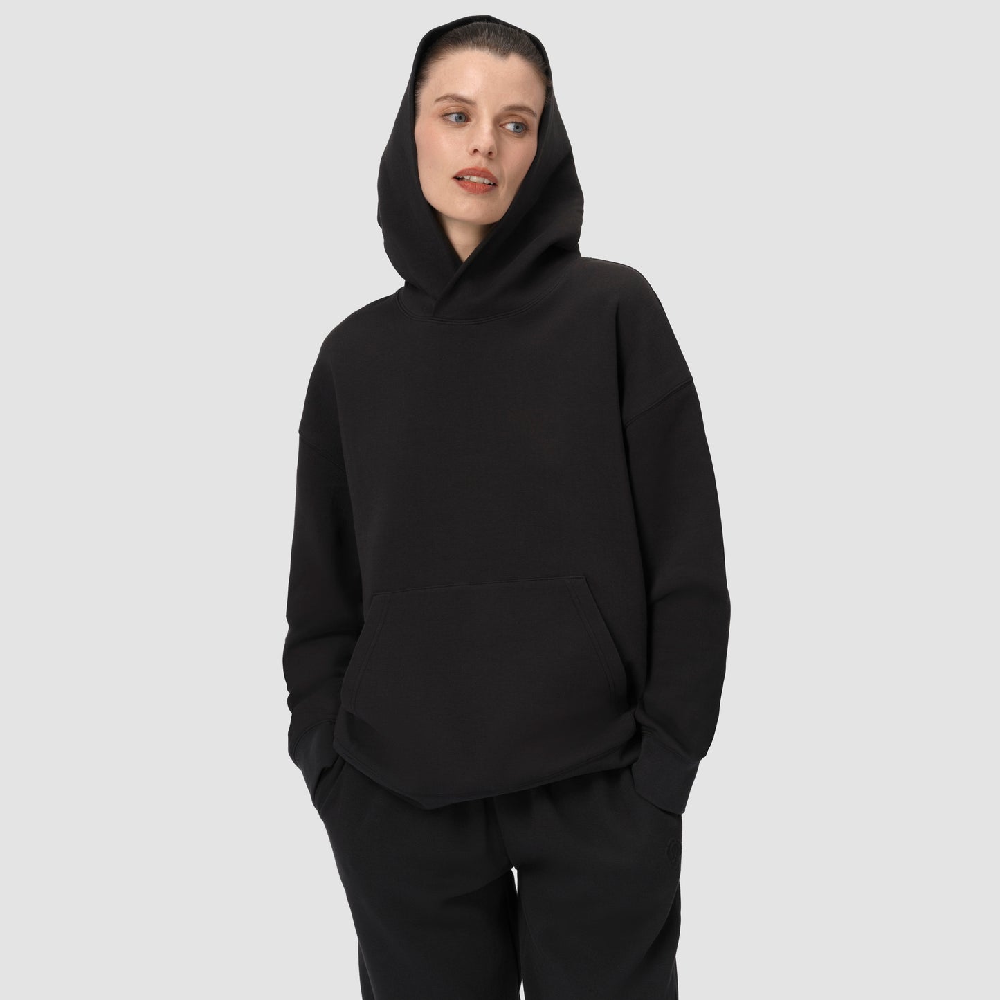 Une personne vêtue d'un sweat à capuche noir et d'un pantalon noir sur un fond uni