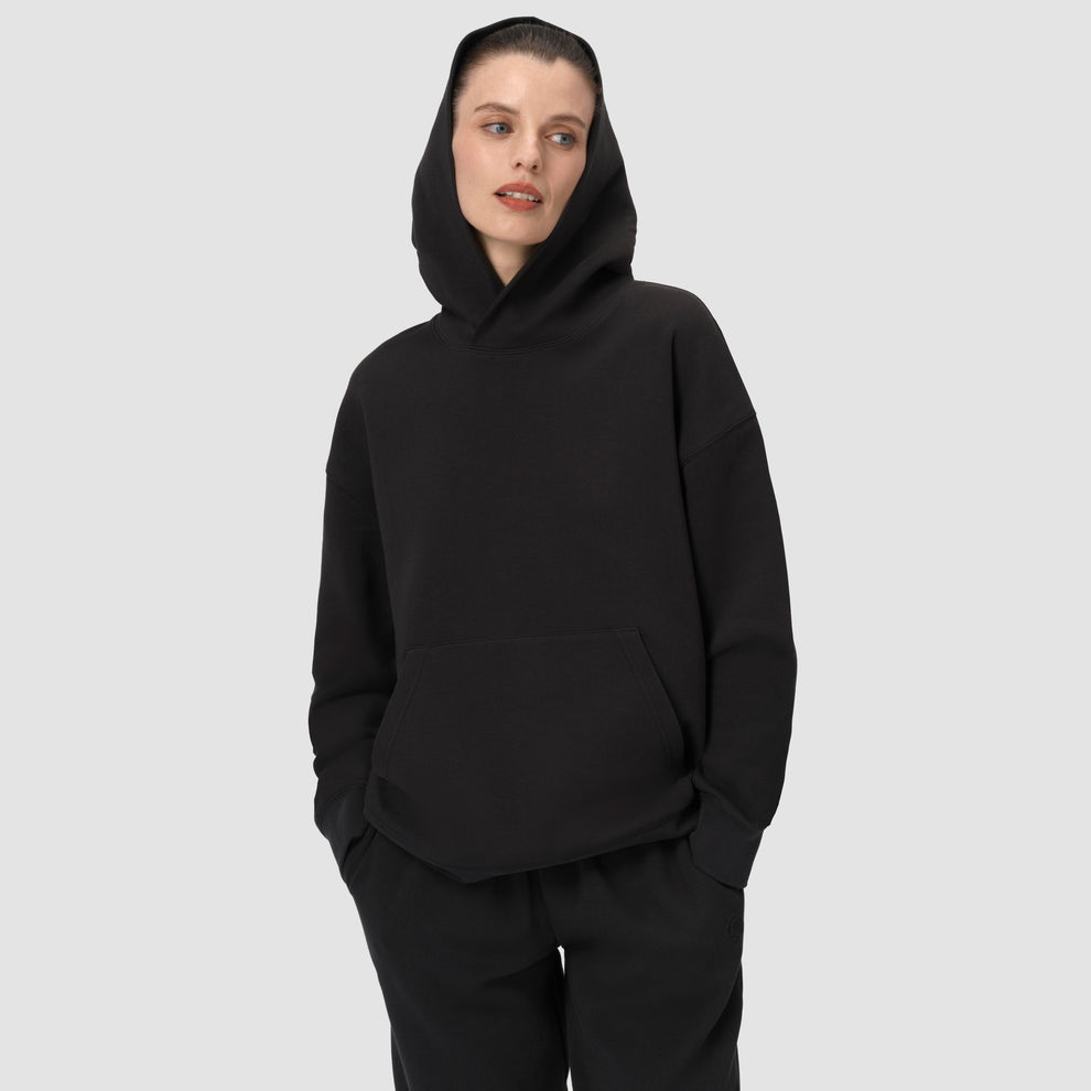 Une personne vêtue d'un sweat à capuche noir et d'un pantalon noir sur un fond uni