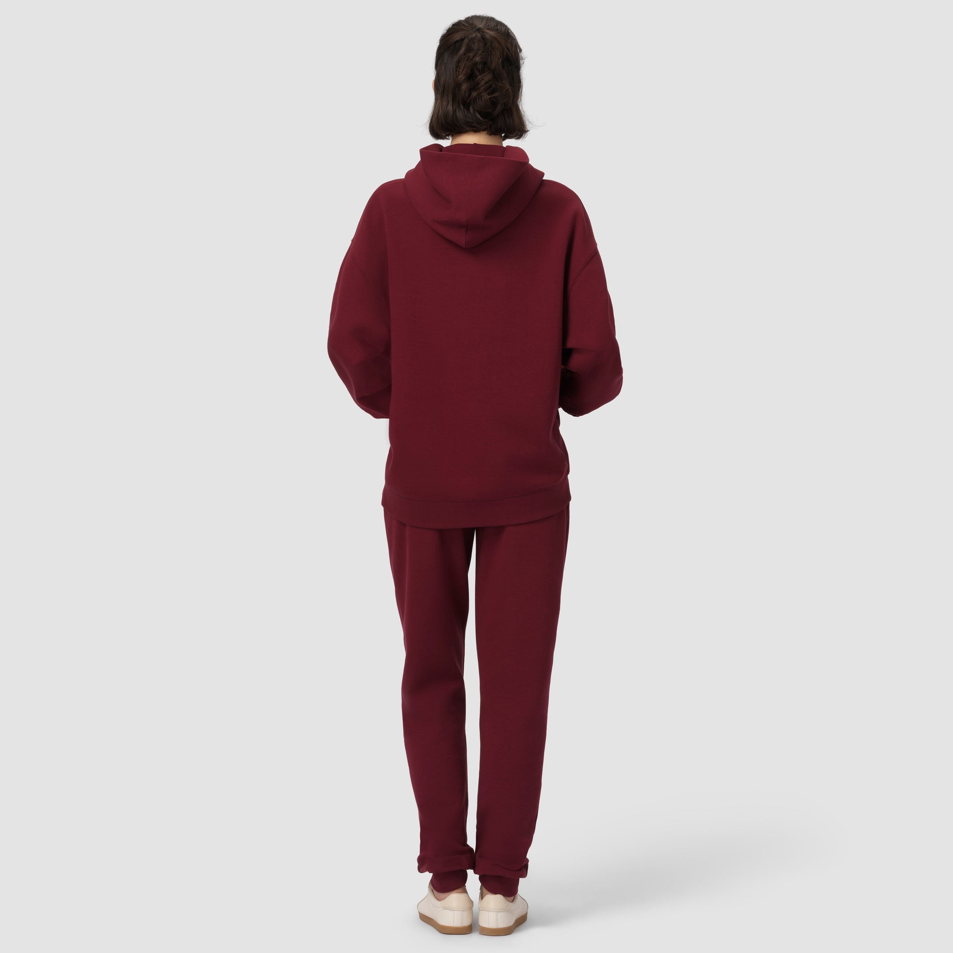 Person wearing a burgundy hoodie and pants on a white background
