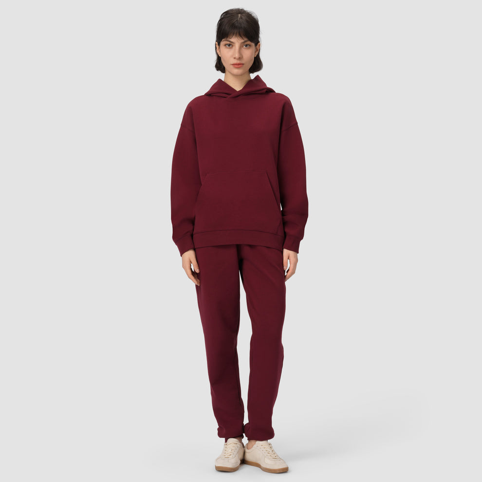 Une personne vêtue d'un ensemble sweat à capuche et pantalon bordeaux sur fond gris clair