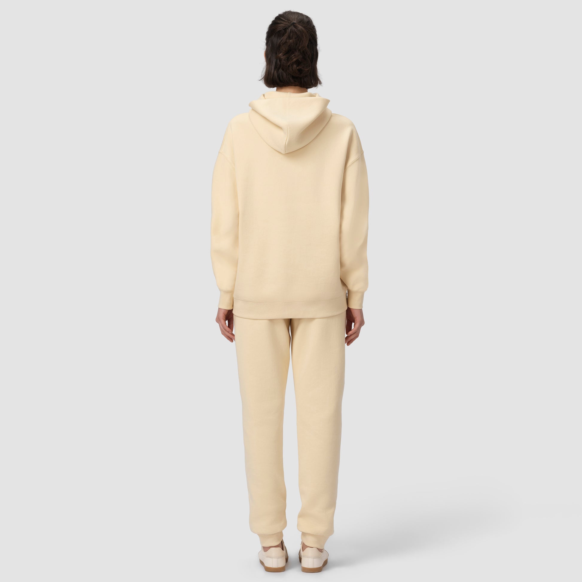 Une personne vêtue d'un sweat à capuche et d'un pantalon de couleur crème sur fond blanc