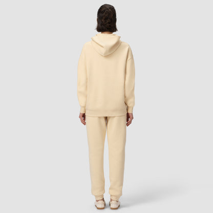 Une personne vêtue d'un sweat à capuche et d'un pantalon de couleur crème sur fond blanc