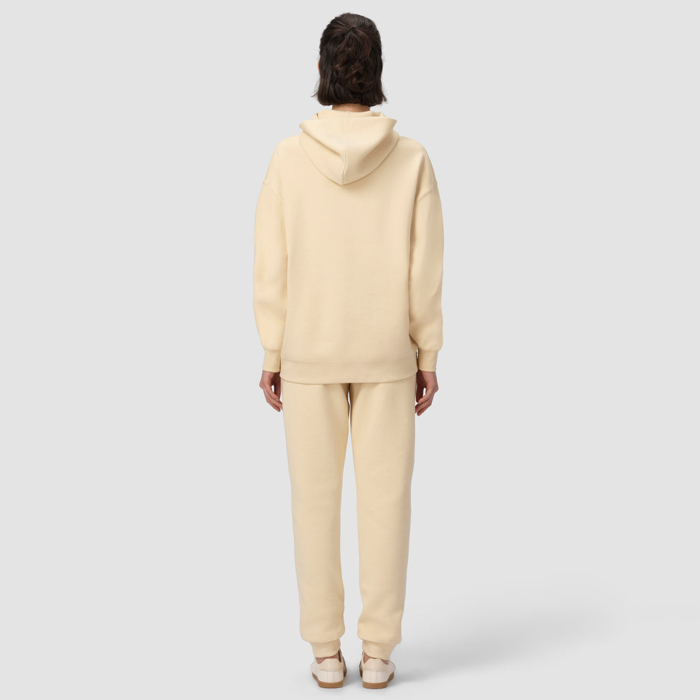 Une personne vêtue d'un sweat à capuche et d'un pantalon de couleur crème sur fond blanc