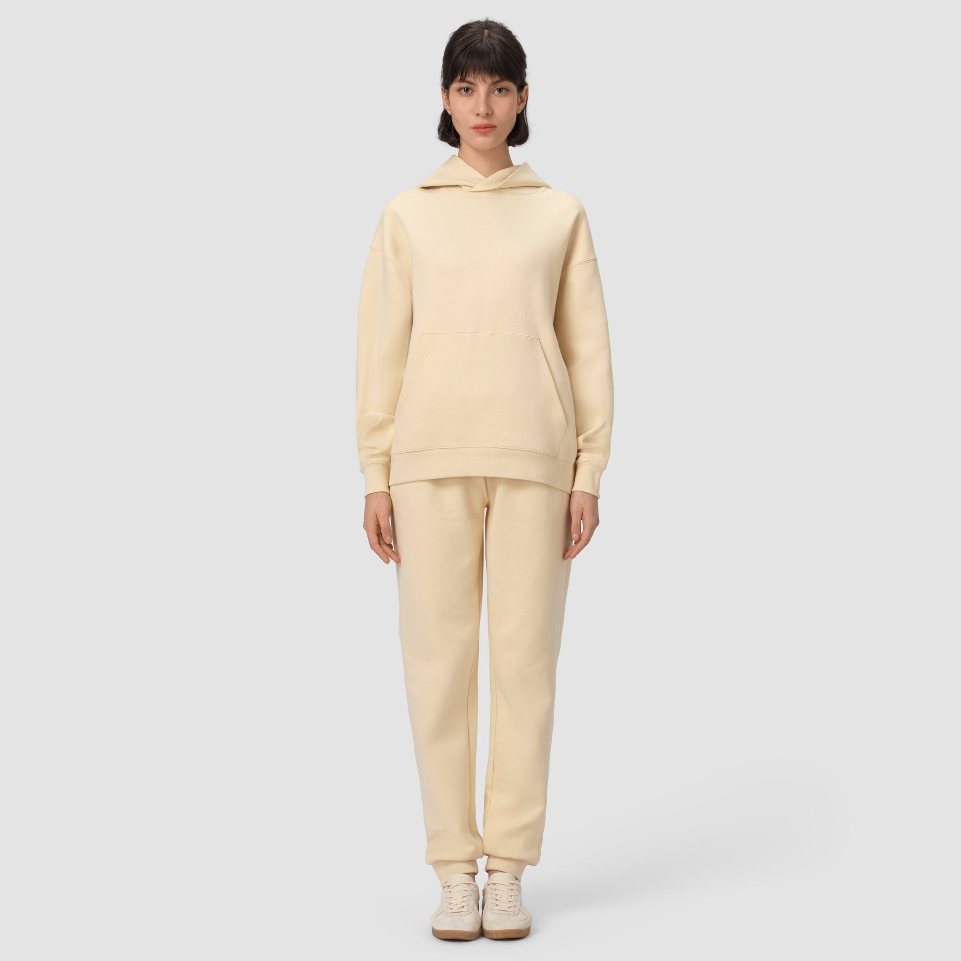 Une personne vêtue d'un ensemble sweat à capuche et pantalon de couleur crème sur un fond gris clair