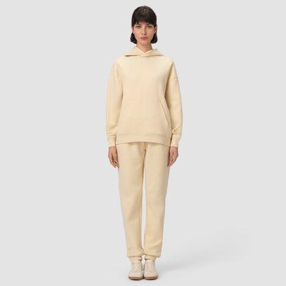 Une personne vêtue d'un ensemble sweat à capuche et pantalon de couleur crème sur un fond gris clair