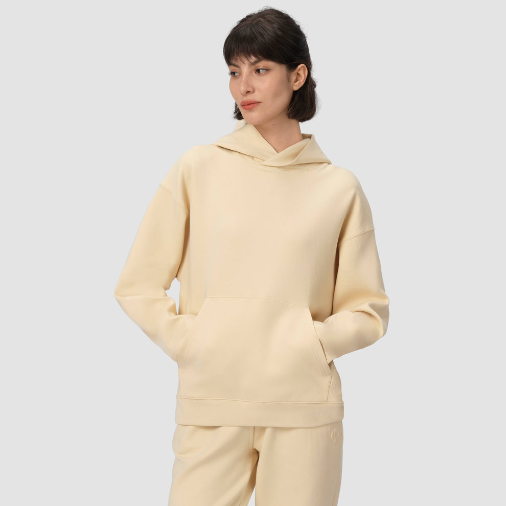 Une personne vêtue d'un sweat à capuche et d'un pantalon de couleur crème sur un fond uni