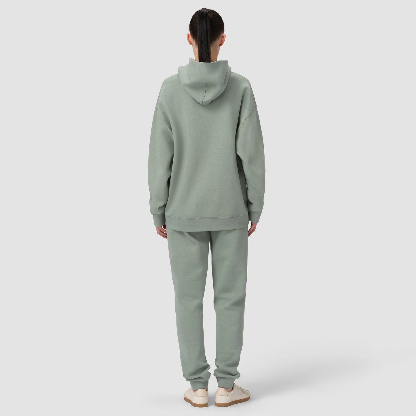 Person wearing a light green hoodie and pants on a white background
