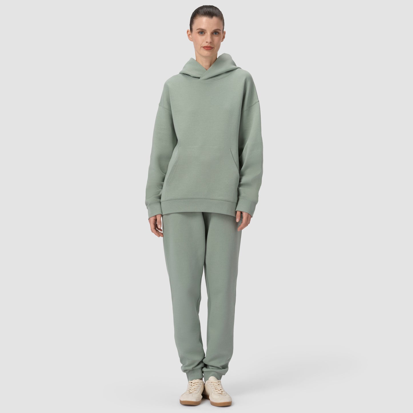 Person wearing a green hoodie and pants set on a light gray background