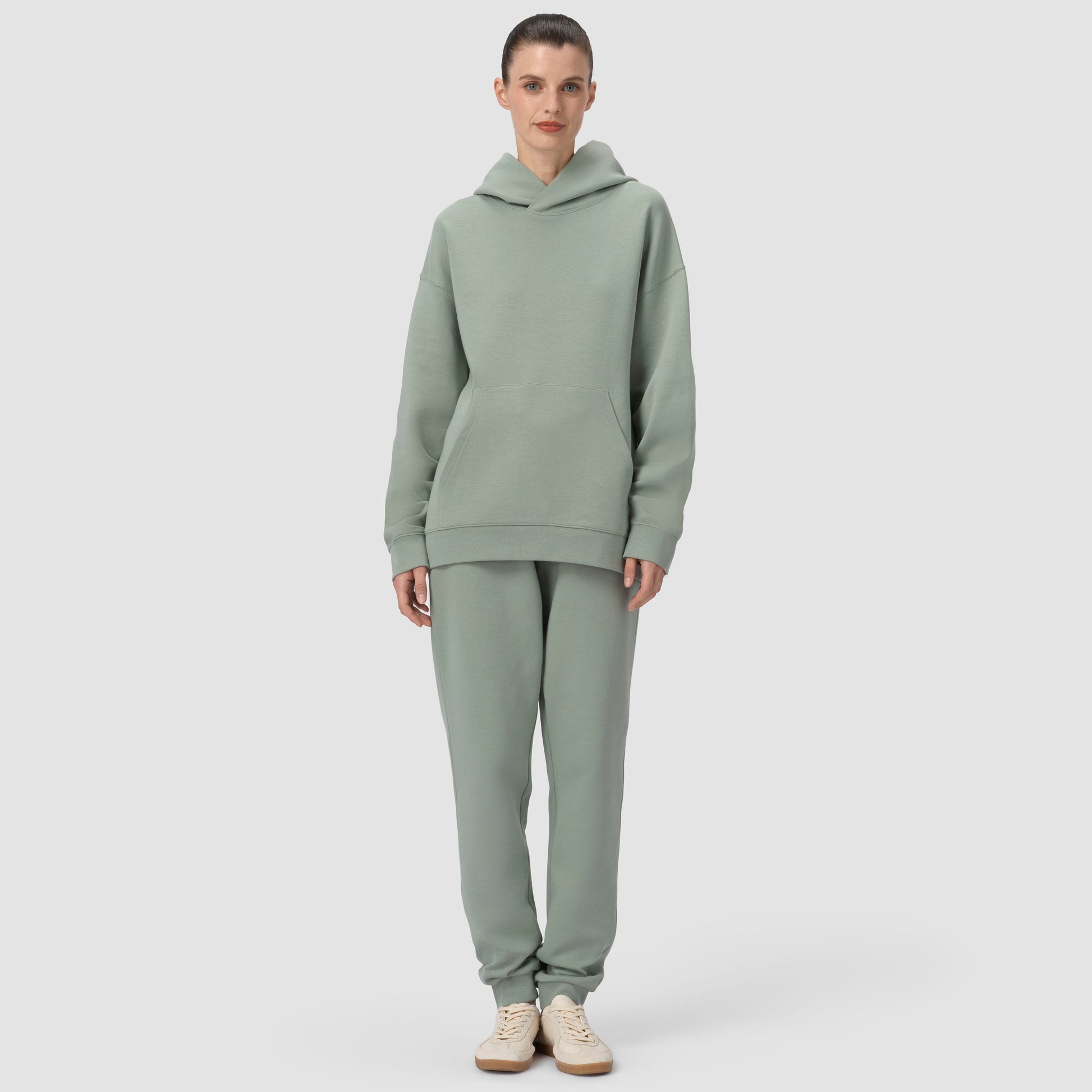 Person wearing a green hoodie and pants set on a light gray background