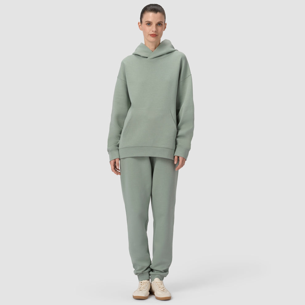 Une personne vêtue d'un ensemble sweat à capuche et pantalon vert sur fond gris clair