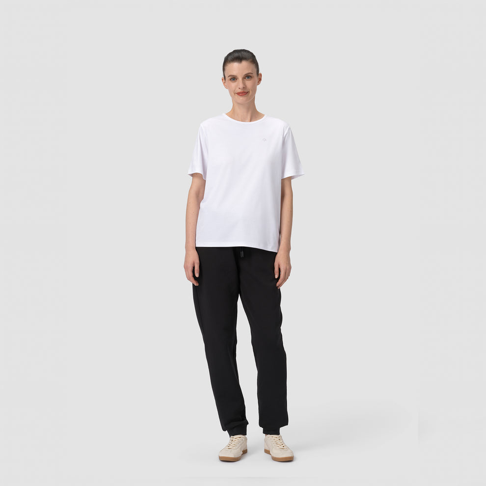 Une personne vêtue d'un t-shirt blanc et d'un pantalon noir sur un fond uni