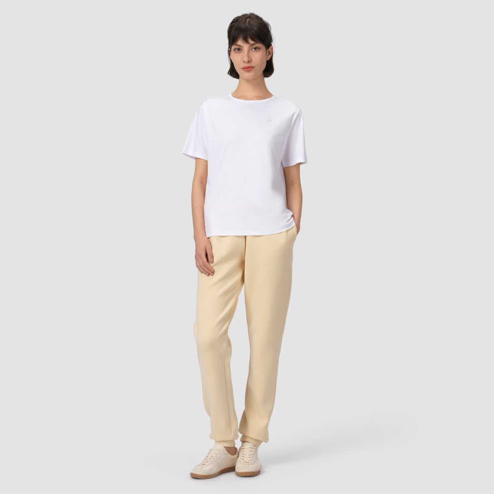 Photo en pied d'un mannequin portant un pantalon de jogging crème, les mains dans les poches, avec un t-shirt blanc et des chaussures 