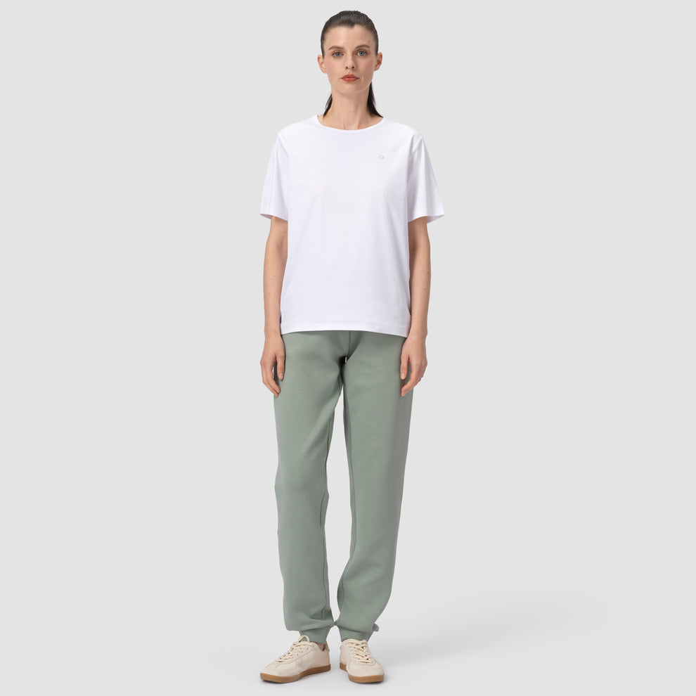 Une personne portant un pantalon de jogging vert sauge, une chemise blanche et des chaussures