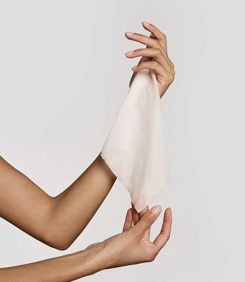 Hands holding a white cotton towelette wet against a plain background