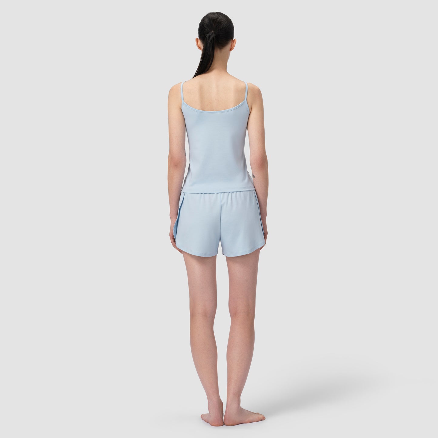 Back of a model wearing a light blue short pajama in plain background