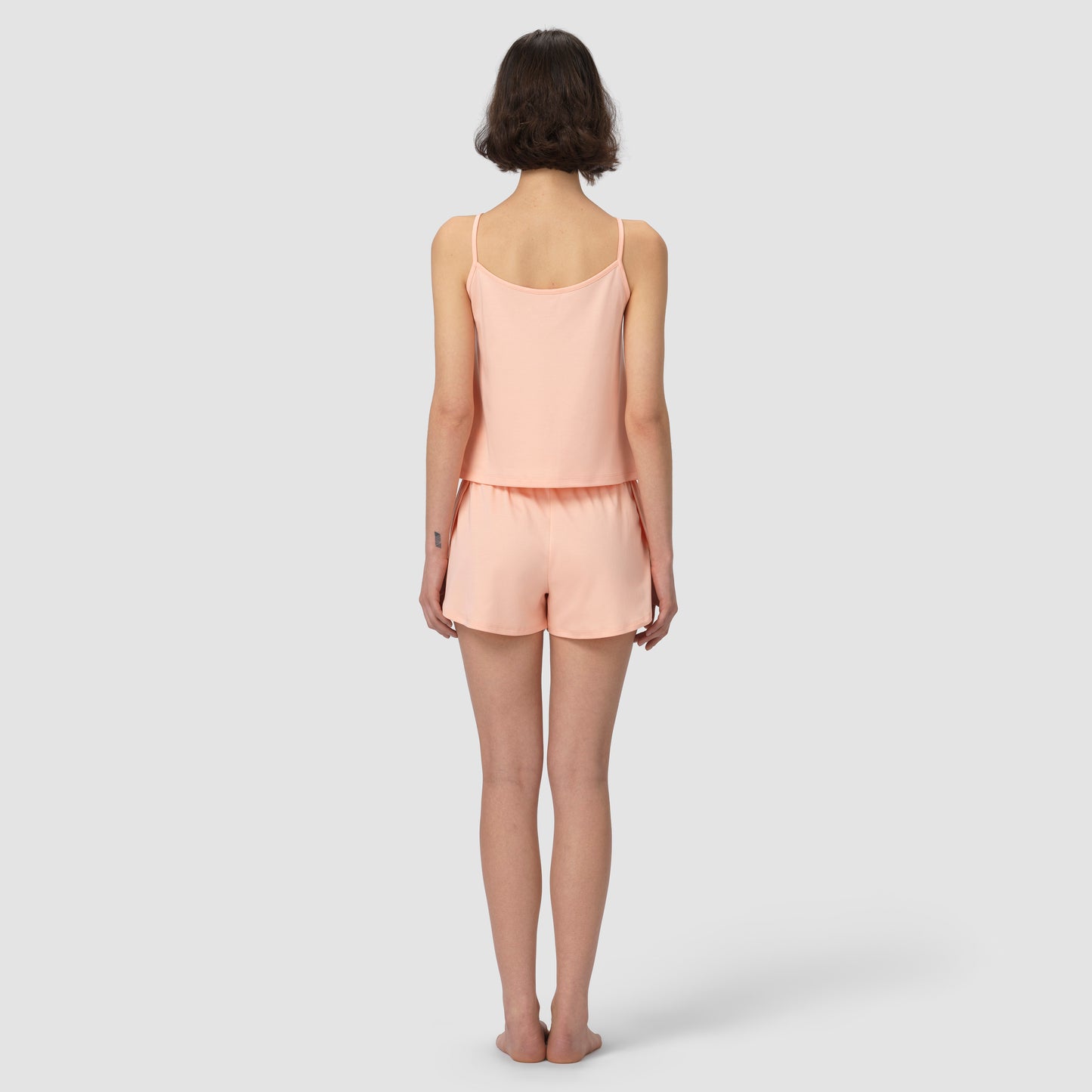 Woman wearing a light pink salmon camisole and shorts set on a white background