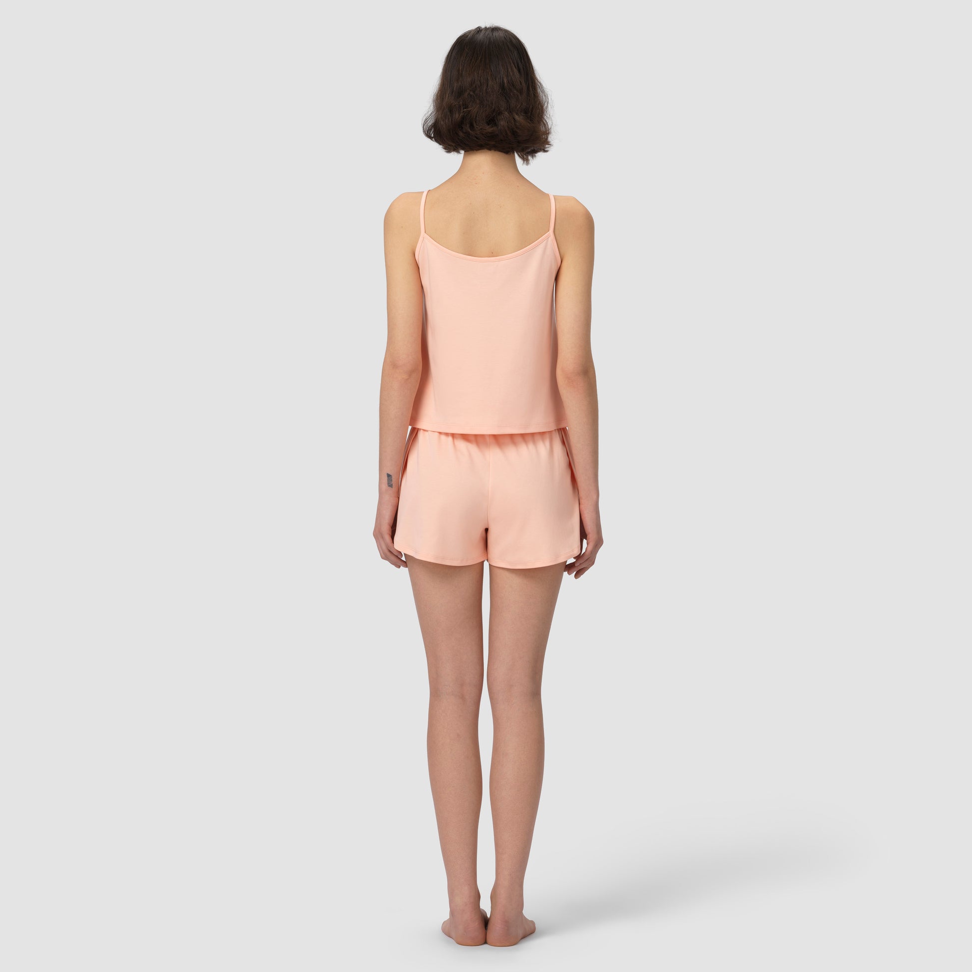 Woman wearing a light pink salmon camisole and shorts set on a white background