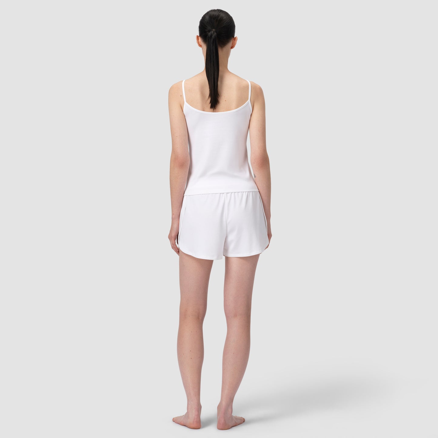 Woman wearing a white tank top and shorts on a plain background