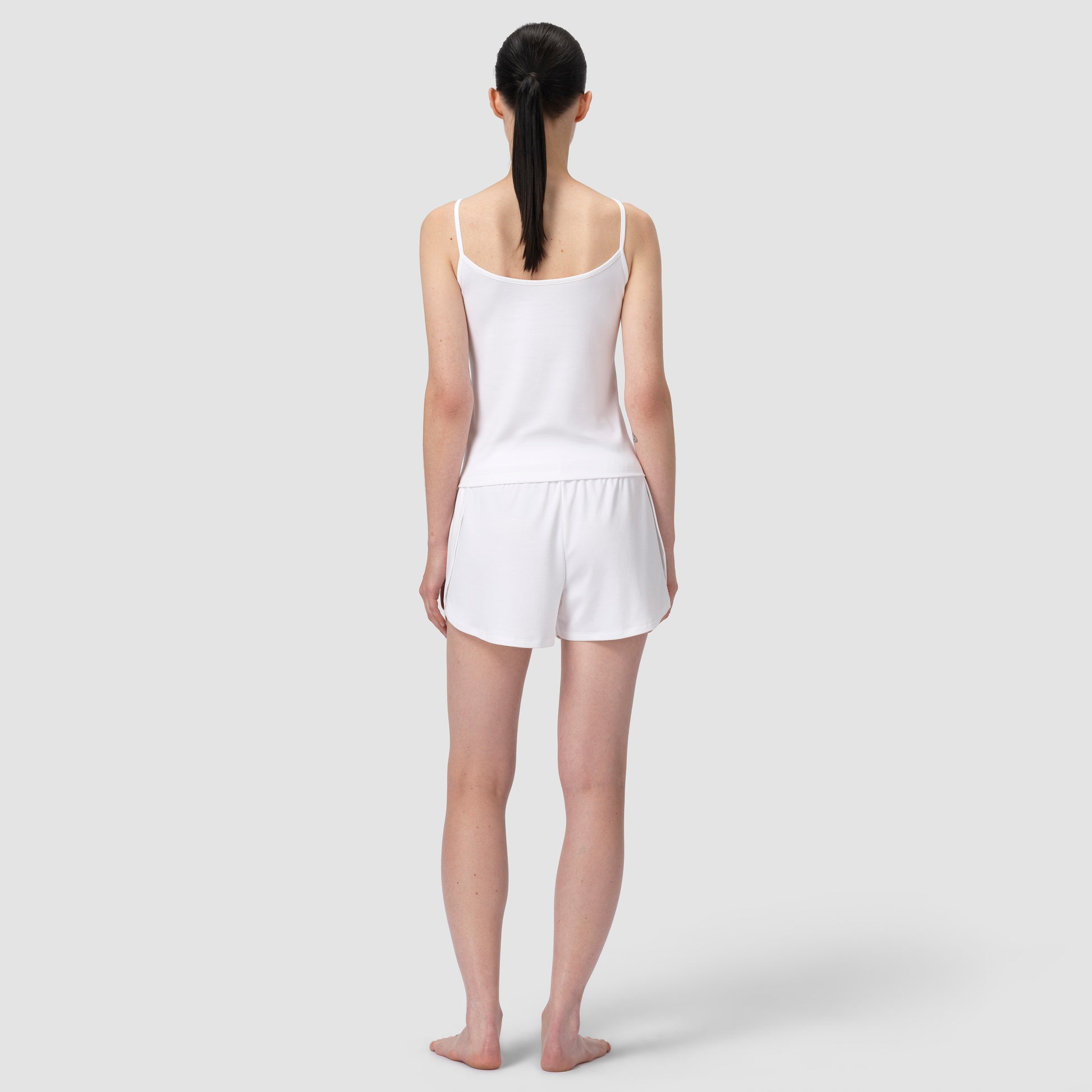 Woman wearing a white tank top and shorts on a plain background