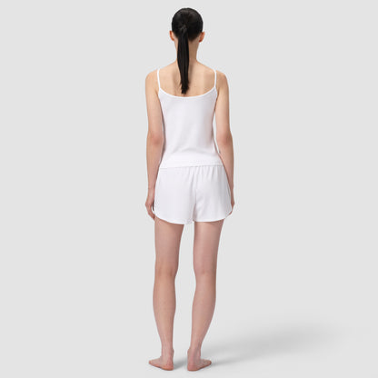 Woman wearing a white tank top and shorts on a plain background