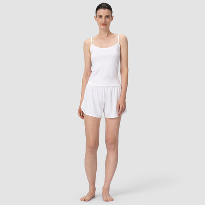 Woman wearing a white tank top and shorts on a plain background