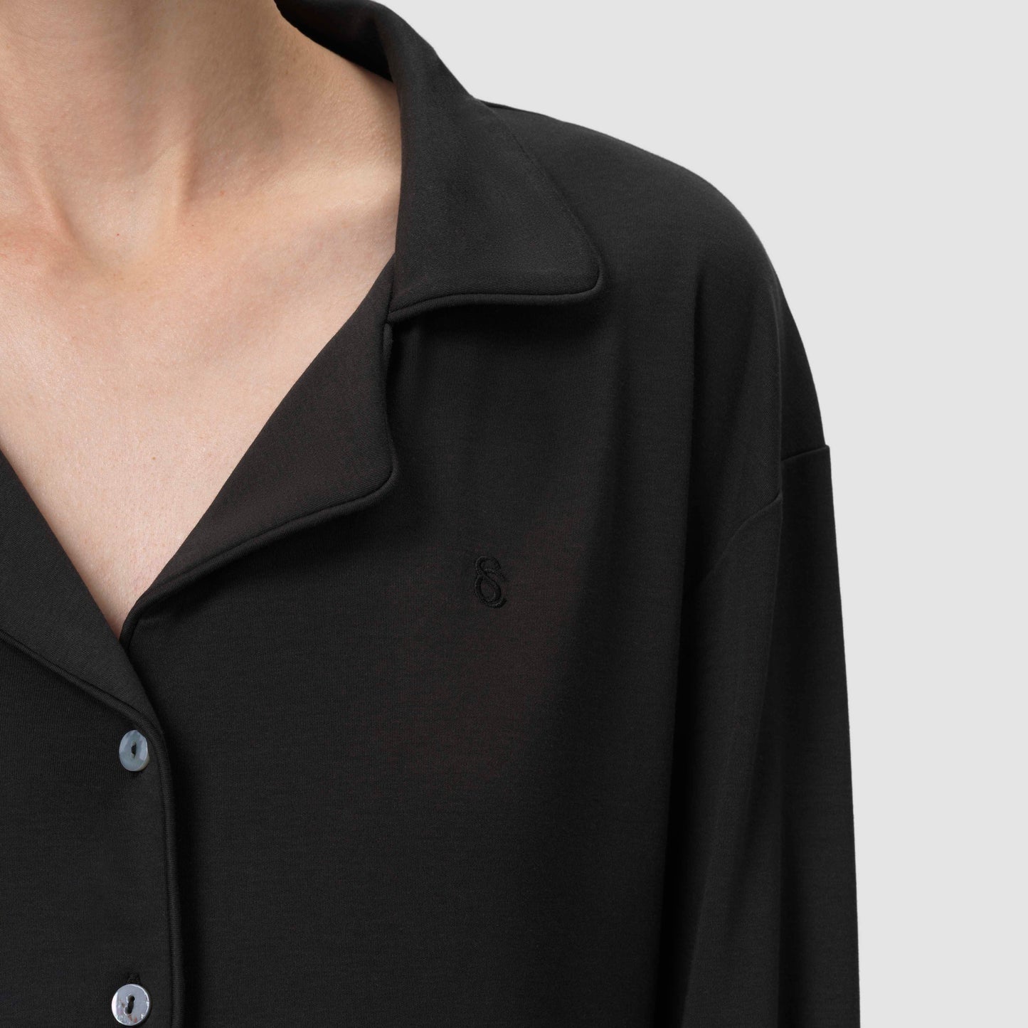 Close-up of a black shirt with a collar and buttons on a light gray background