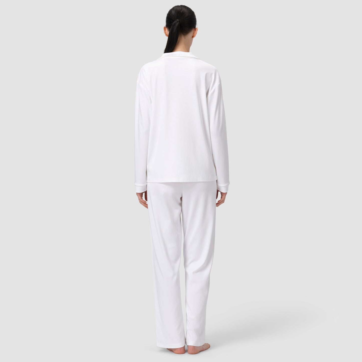 Back shot of model in white pajama set in plain background