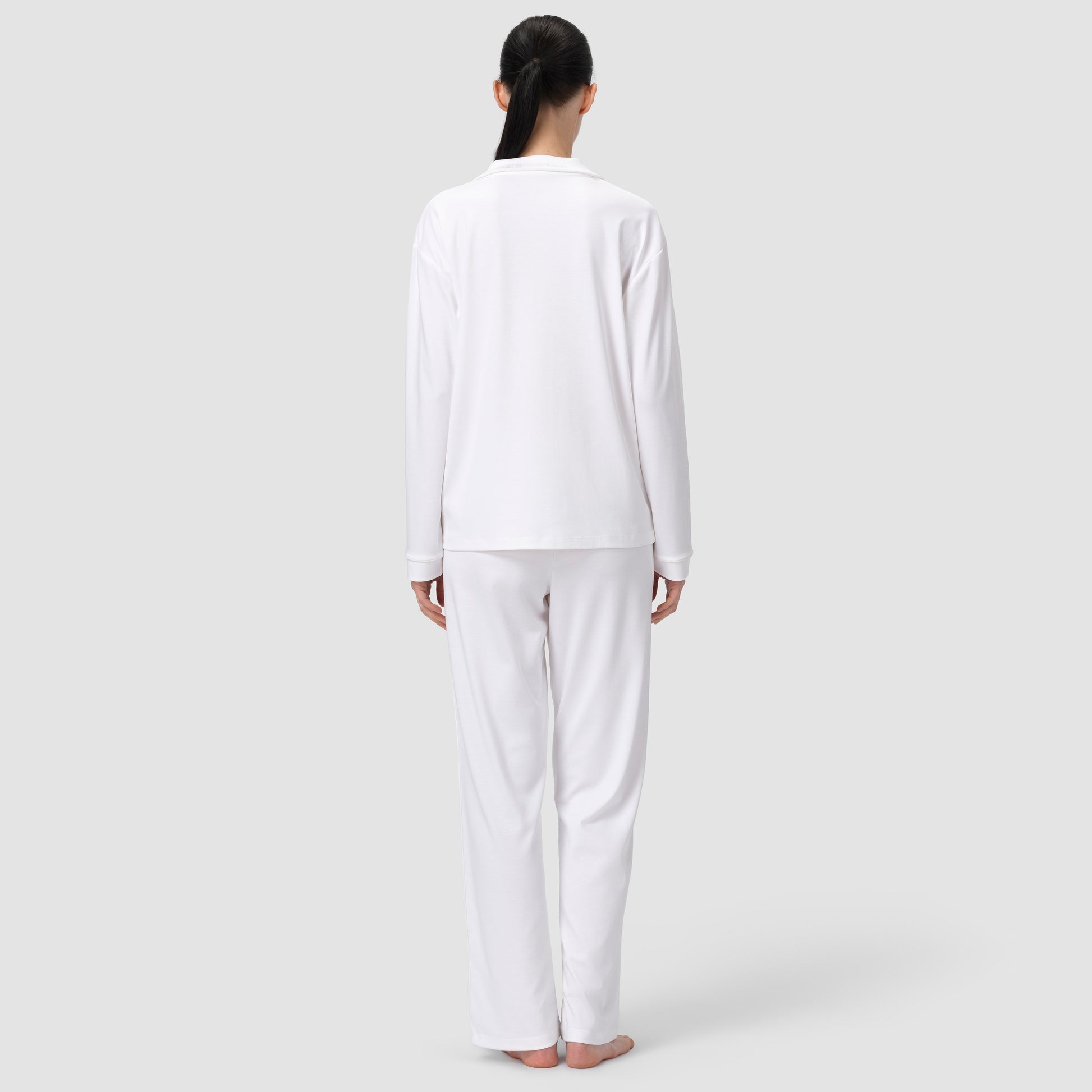 Back shot of model in white pajama set in plain background