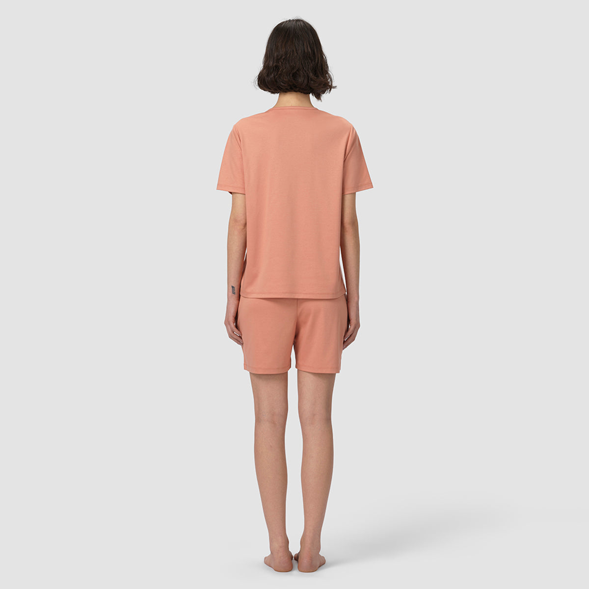 Person wearing a matching peach-colored t-shirt and shorts set on a white background