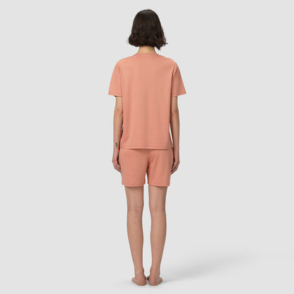 Person wearing a matching peach-colored t-shirt and shorts set on a white background