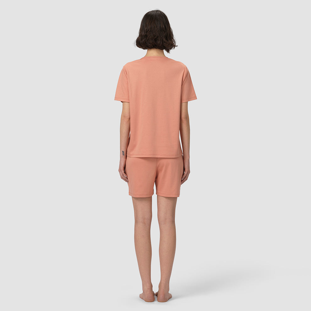 Une personne portant un ensemble t-shirt et short assortis de couleur pêche, sur fond blanc
