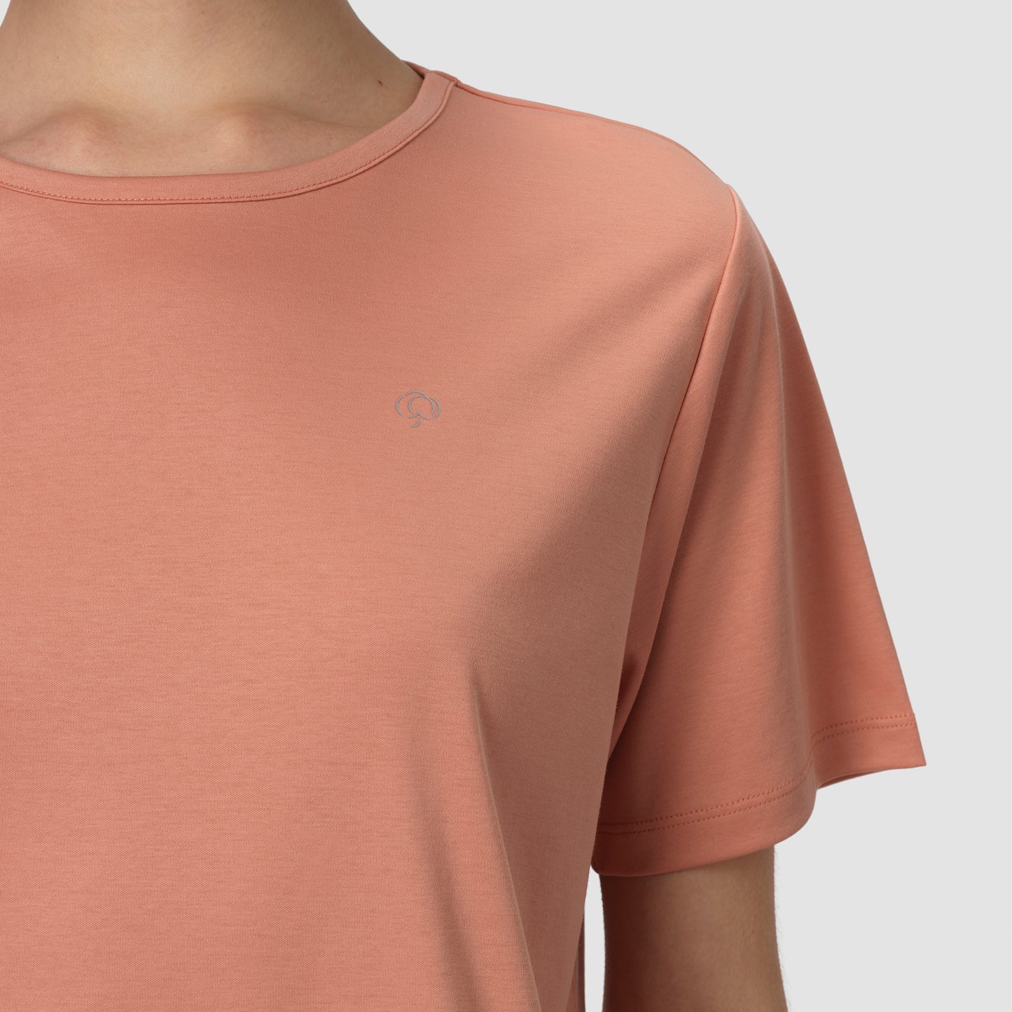 Close-up of a person wearing a terracotta-colored t-shirt with a small logo on a light gray background