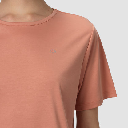 Close-up of a person wearing a terracotta-colored t-shirt with a small logo on a light gray background