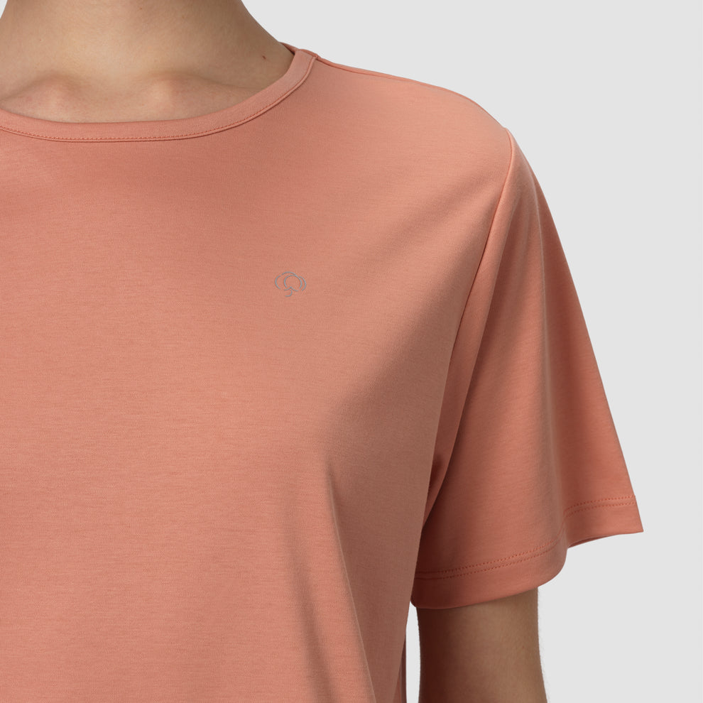 Gros plan sur une personne portant un t-shirt couleur terre cuite orné d'un petit logo sur fond gris clair