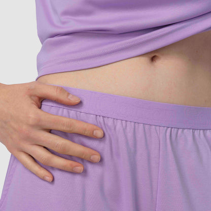 Person wearing a light purple pajama with a hand on their hip against a white background