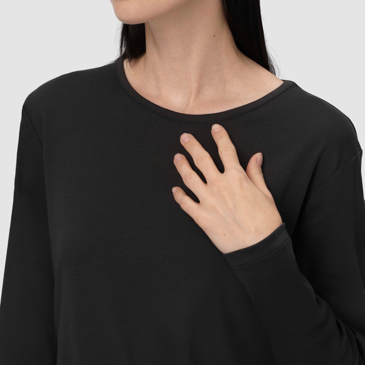 Person wearing a black long-sleeve shirt with a plain background