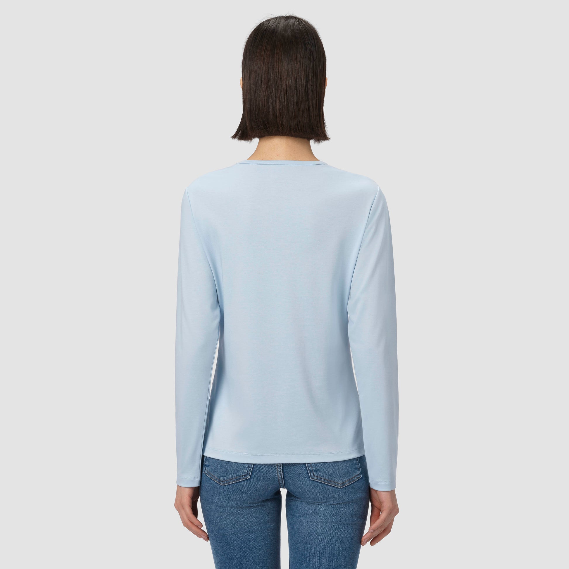 Person wearing a light blue long-sleeve shirt and blue jeans on a plain background