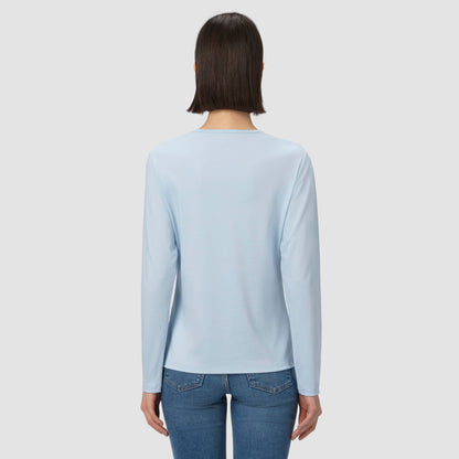 Person wearing a light blue long-sleeve shirt and blue jeans on a plain background