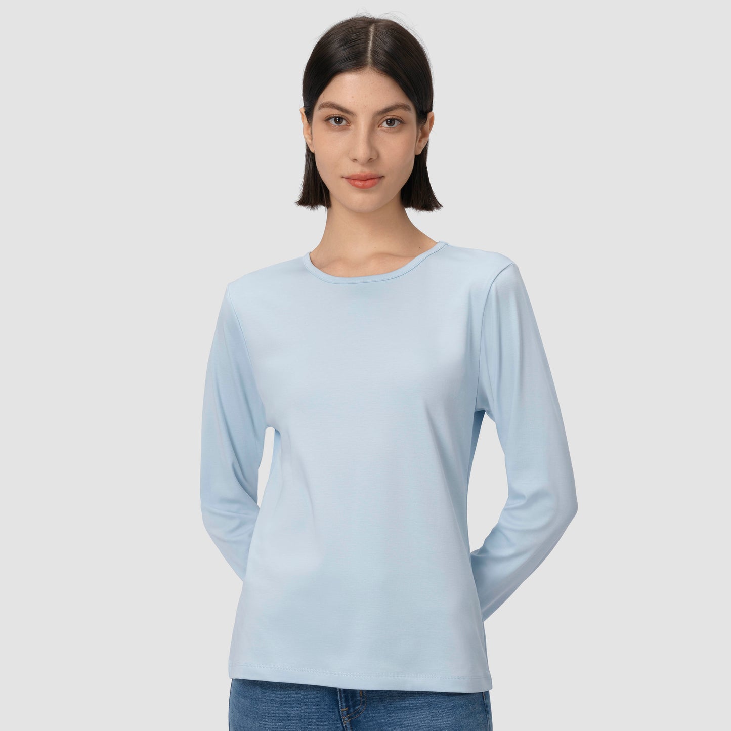 Woman wearing a light blue long-sleeve shirt against a plain background