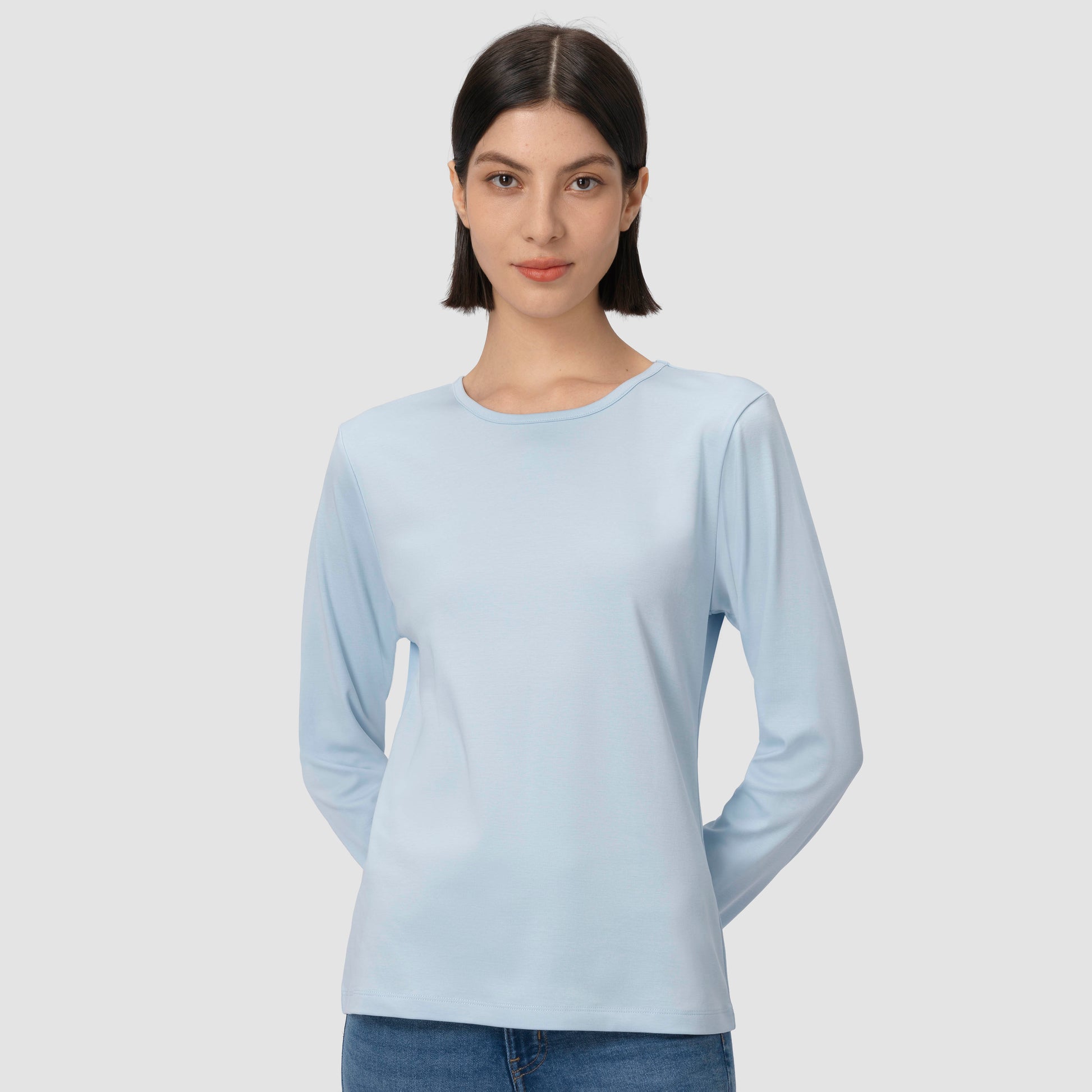 Woman wearing a light blue long-sleeve shirt against a plain background