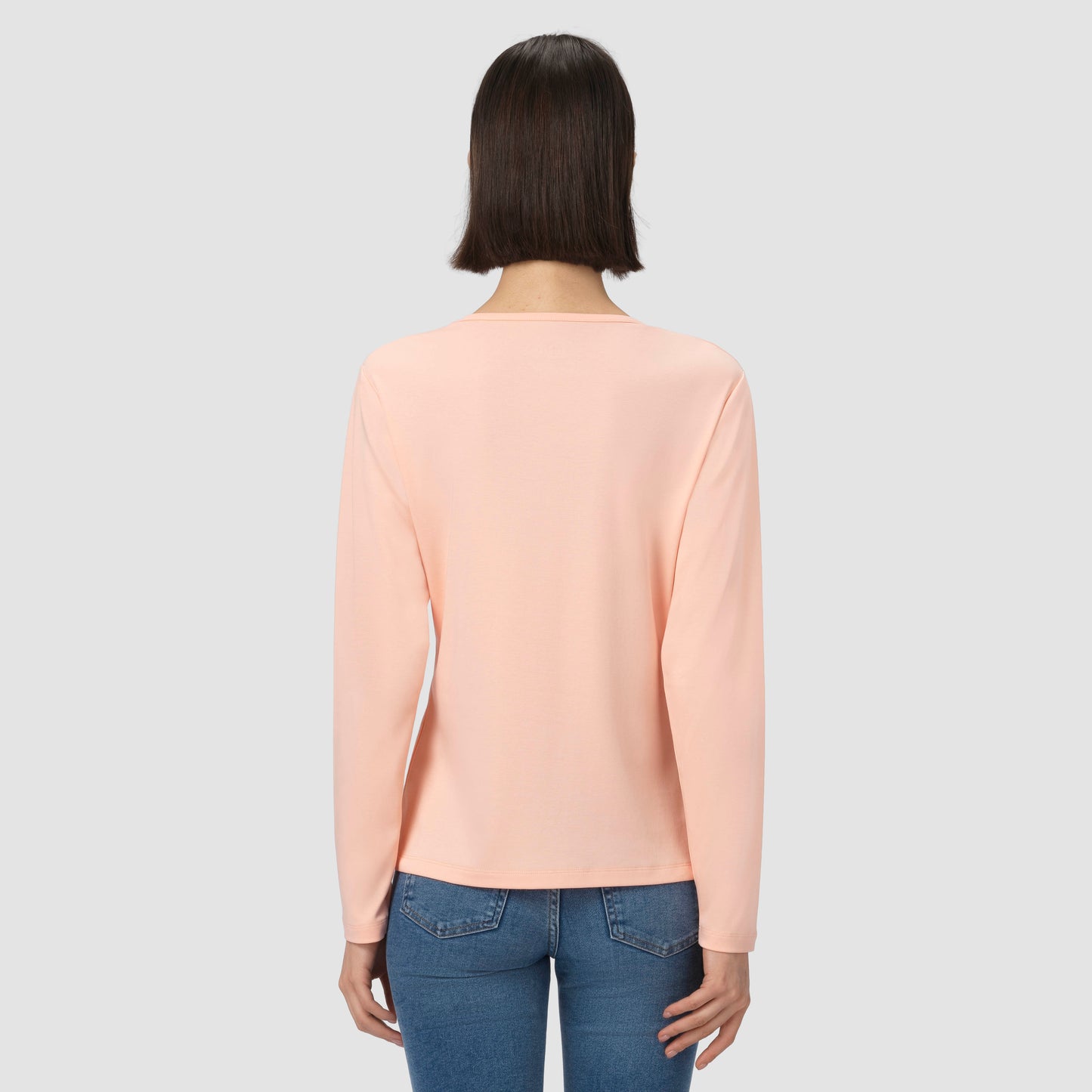 Person wearing a light pink shirt and blue jeans on a plain background